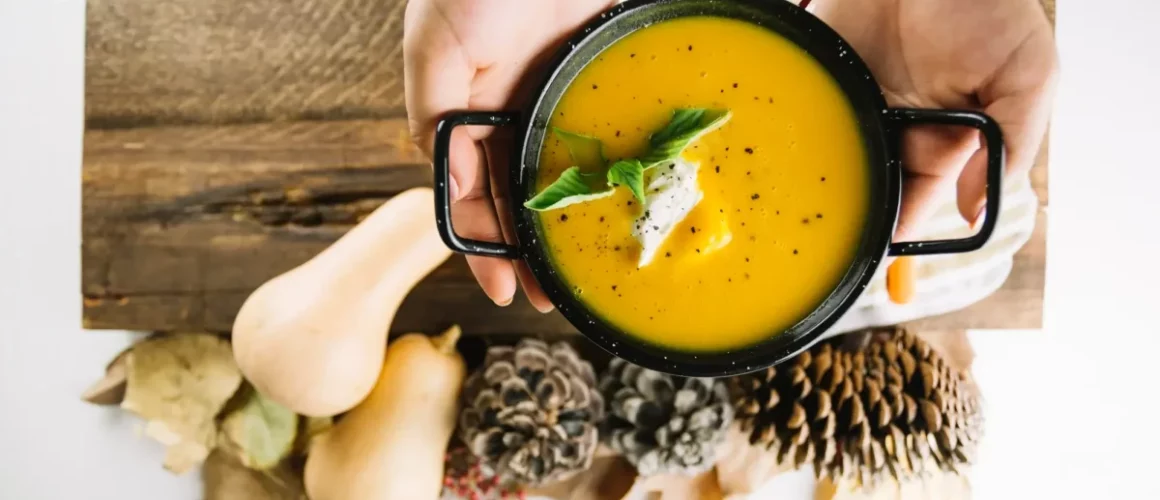 Creamy carrot and caraway soup with fresh parsley in a rustic ceramic bowl on a wooden table.